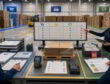 Warehouse team reviews corrugated box storage roles, pallet checks, and quality holds at a shared control desk.