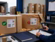 Warehouse worker documents kraft paper roll inspection beside a delivery truck, flagging one damaged roll.