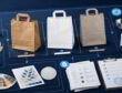 Procurement desk comparing kraft, white, and recycled paper bags with testing, print, and compliance checks.