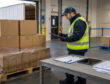 Warehouse worker inspecting a pallet of damp corrugated boxes at a loading dock before storage.