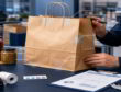 Quality inspector examines a kraft paper bag at a checkout desk with failure-point callouts and retail packaging tools.