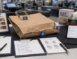 Retail evidence desk with torn paper bag, failure markers, clipboards, and tablet for checkout incident review.